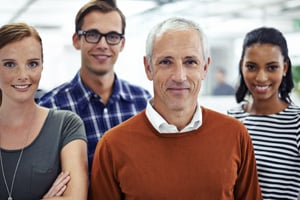 Mature MBA student in orange sweater standing in a group with three younger classmates and smiling