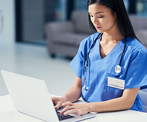 RN in blue scrubs learning online using laptop computer