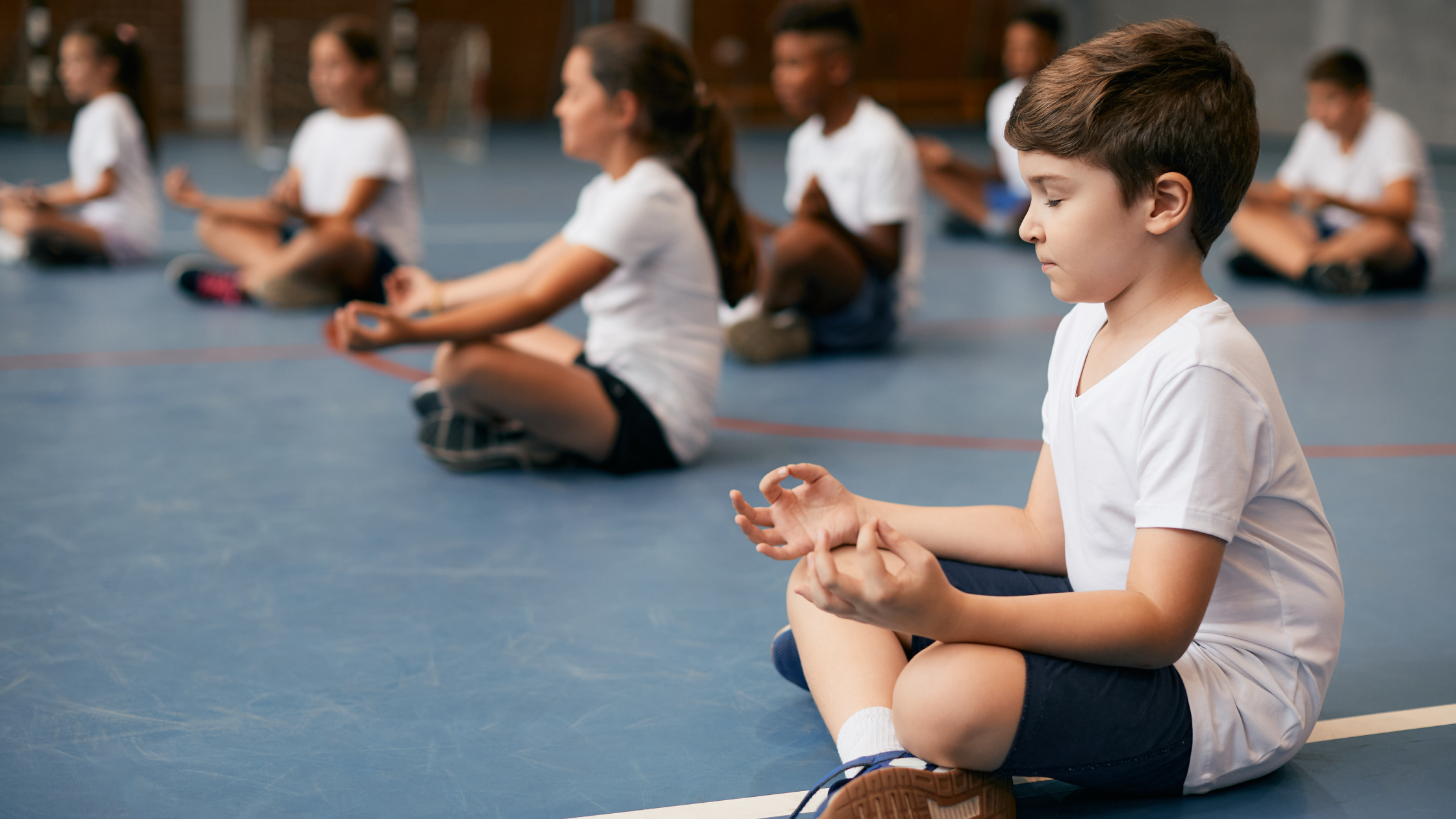 Children sitting cross-legged in a gym practicing meditation during a mindfulness exercise.