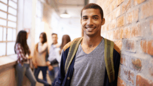 Smiling college student with backpack standing in brick hallway with classmates in background