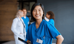 Confident healthcare professional in blue scrubs smiles with medical team in hospital corridor background