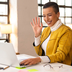 Businesswoman in yellow jacket waving at her laptop screen