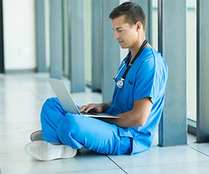 Nurse seated on the floor of a hallway working on a laptop